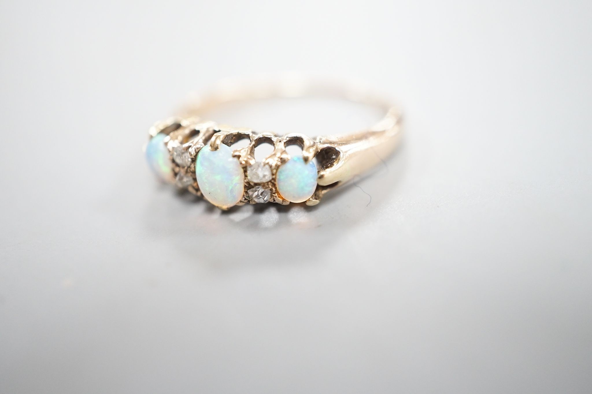 An early 20th century yellow metal three stone white opal and four stone diamond chip set half hoop ring, size M, gross weight 2.6 grams.